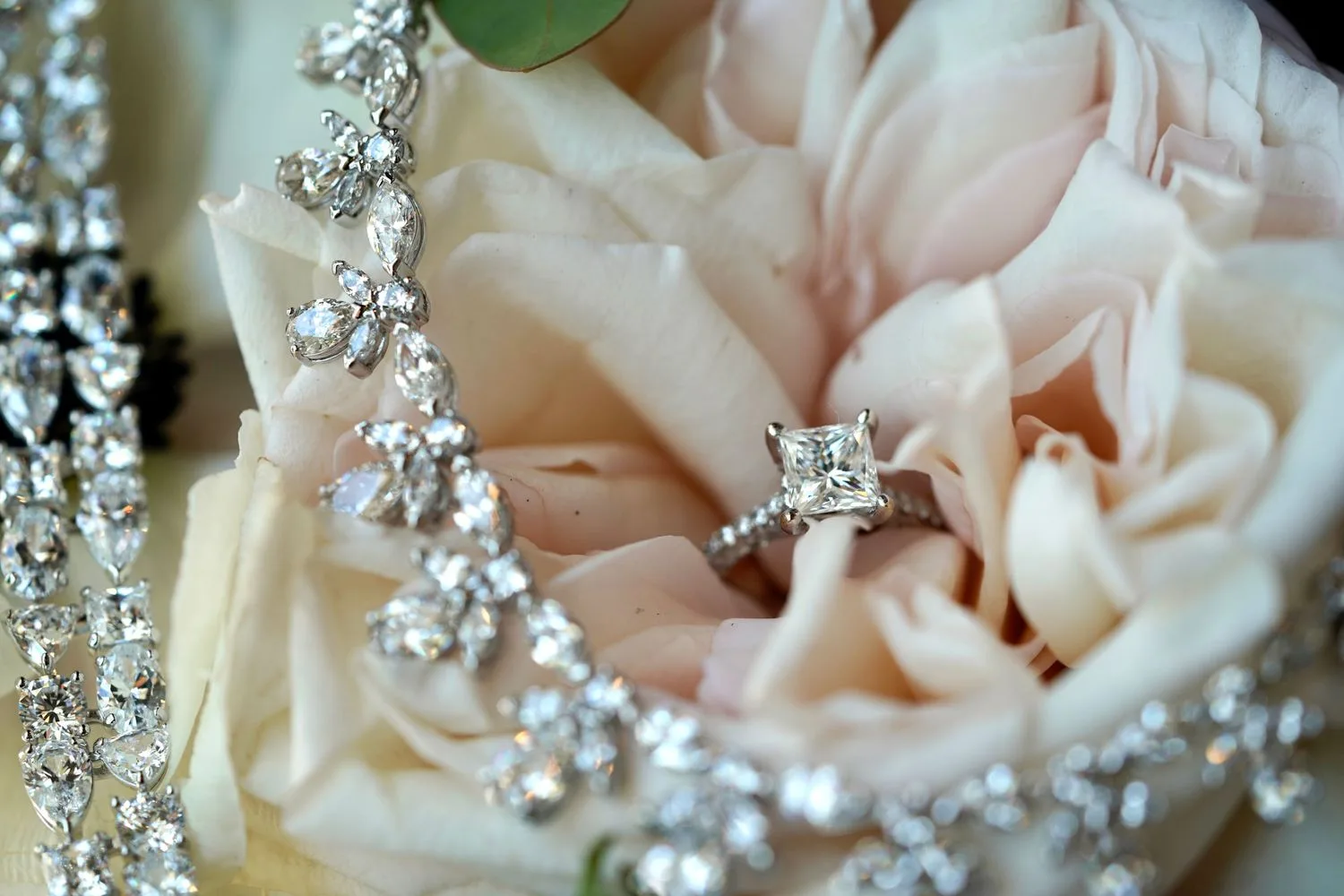 Princess-cut engagement ring and diamond necklace resting on a blush rose — Maximus Visions wedding photography, New Jersey & New York City