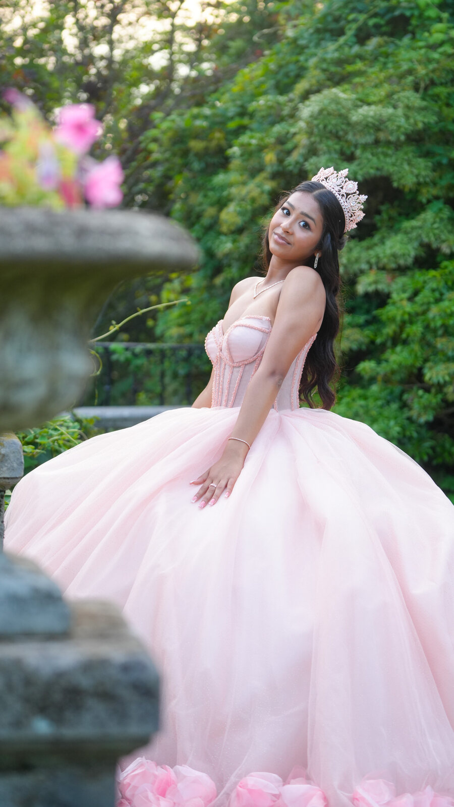Quinceañera in a pink gown looking toward the camera beside a garden urn