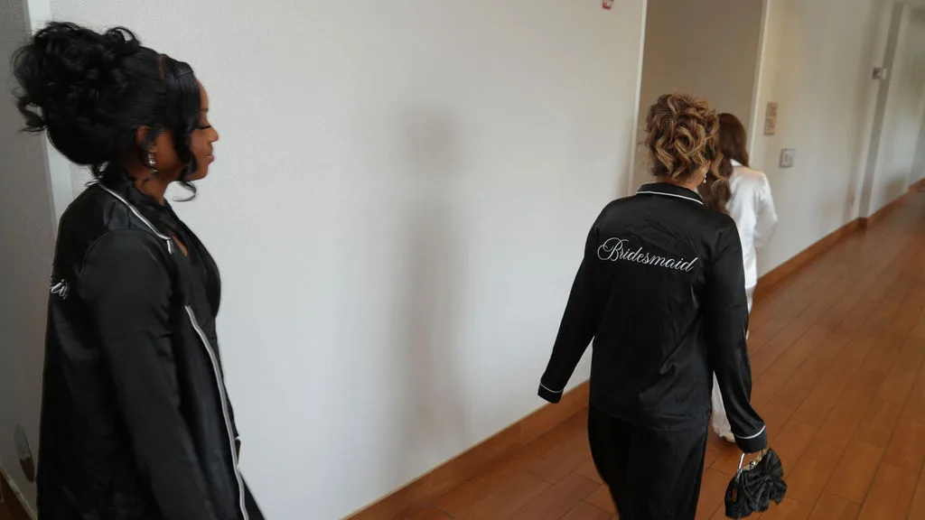 Bridesmaids in embroidered robes walk the hotel hallway on the wedding morning, New Jersey