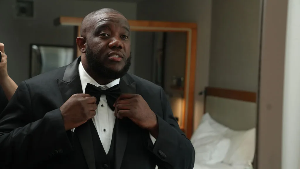 Tre adjusts his bow tie with a smile in the hotel suite — groom getting-ready photography, New Jersey
