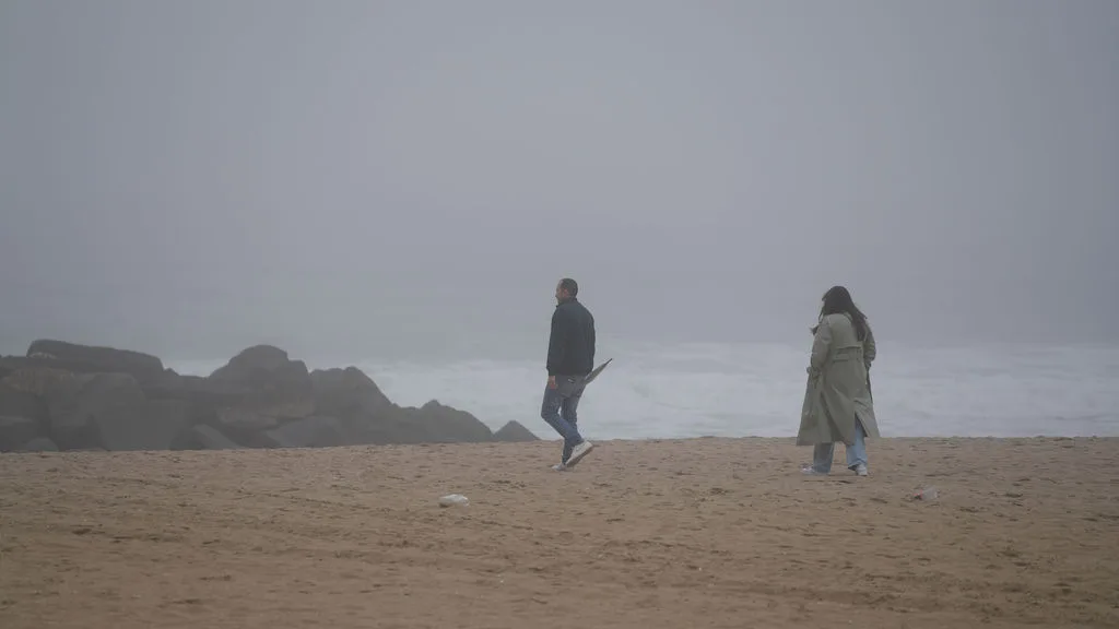 He carries a clear umbrella as they walk the misty shoreline together — documentary proposal session, New Jersey