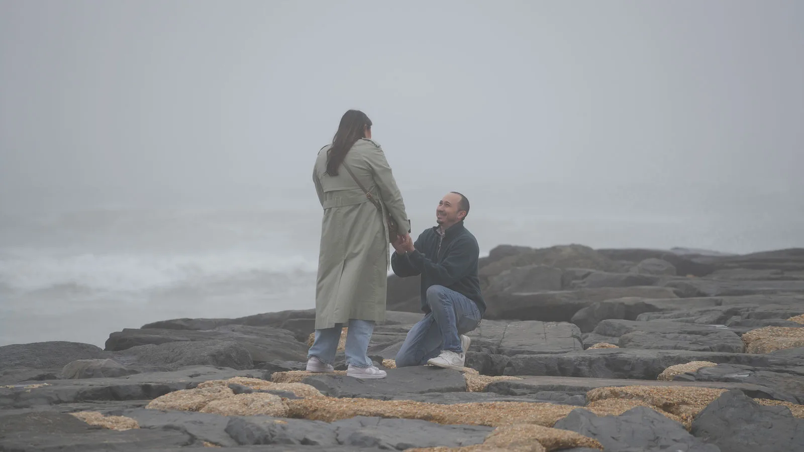 The proposal — he kneels on the fog-covered jetty holding the ring up to her, the grey ocean stretching behind them, New Jersey shore