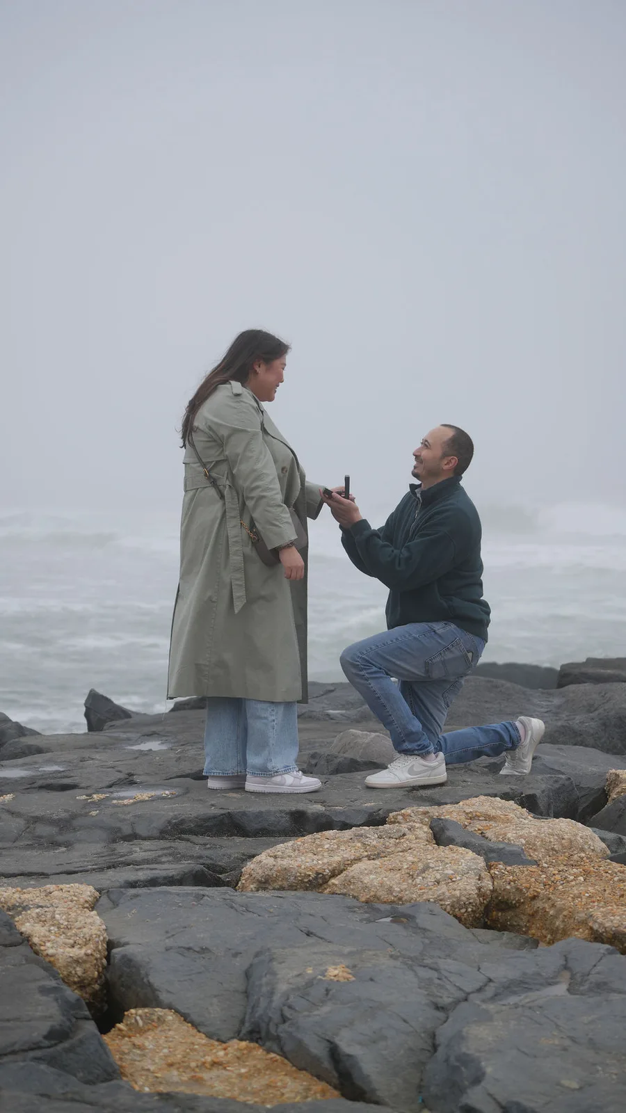 Her smile breaking through the shock as he kneels with the ring — candid proposal reaction, New Jersey shore