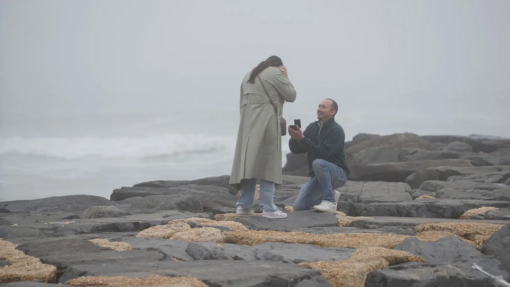 Overwhelmed on the jetty, hands over her mouth, the ocean roaring behind — surprise proposal, New Jersey