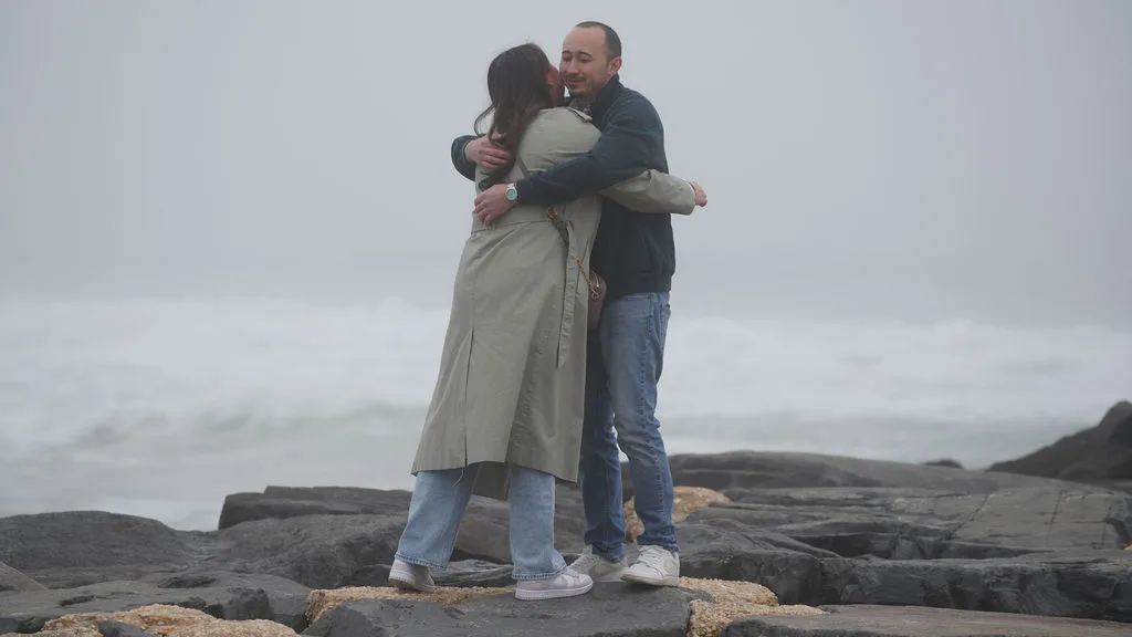 Holding each other tight against the sea mist, newly engaged — New Jersey shore
