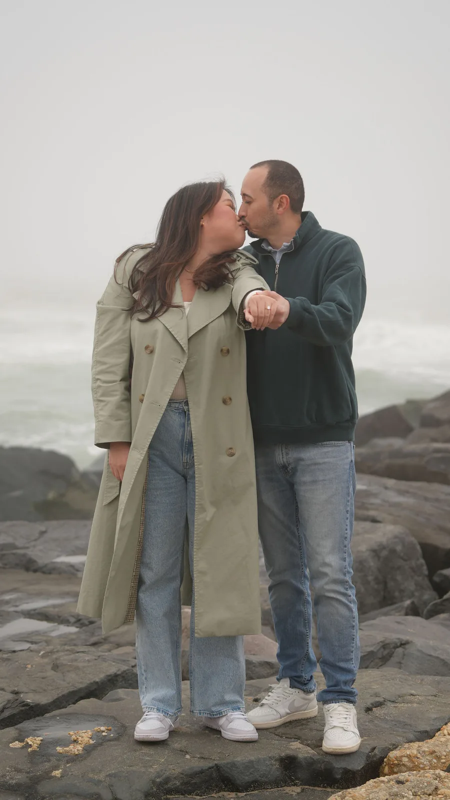 A kiss on the jetty rocks as she holds out her hand with the new ring, fog and surf behind them — Maximus Visions, New Jersey